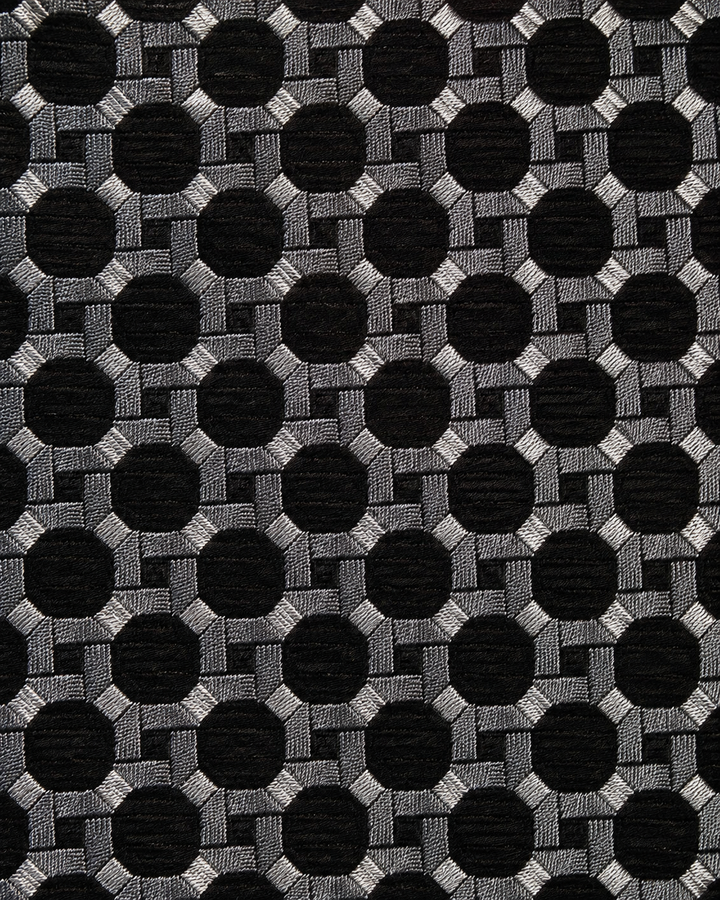 Närbild av tätt geometriskt galler av silver- och svartfärgade ringar och cirklar på AXEL, bred slips i svart och silver