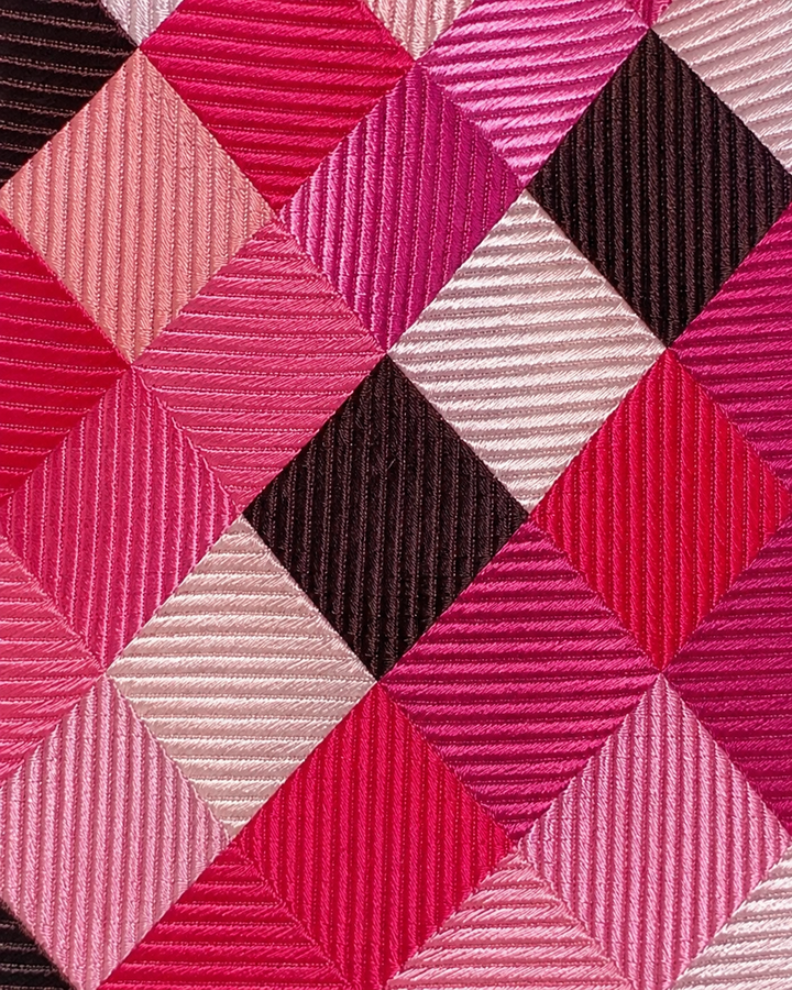 Närbild av stora argyle- och rutformer över en randig struktur på ESTELLINE, bred slips i rosa, svart och silver