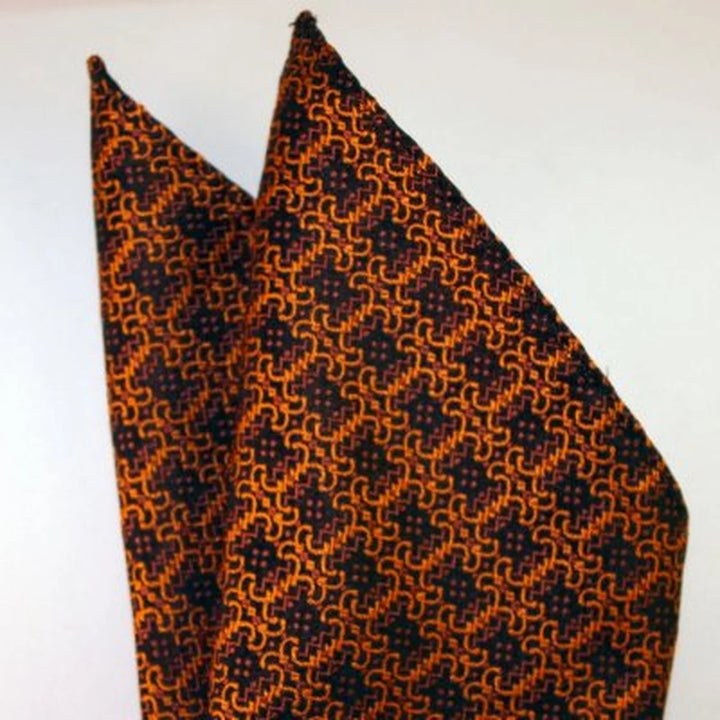 FURINA, bröstnäsduk i svart och orange med ett tätt sammanlänkat orange geometriskt motiv på svart botten – originalbild