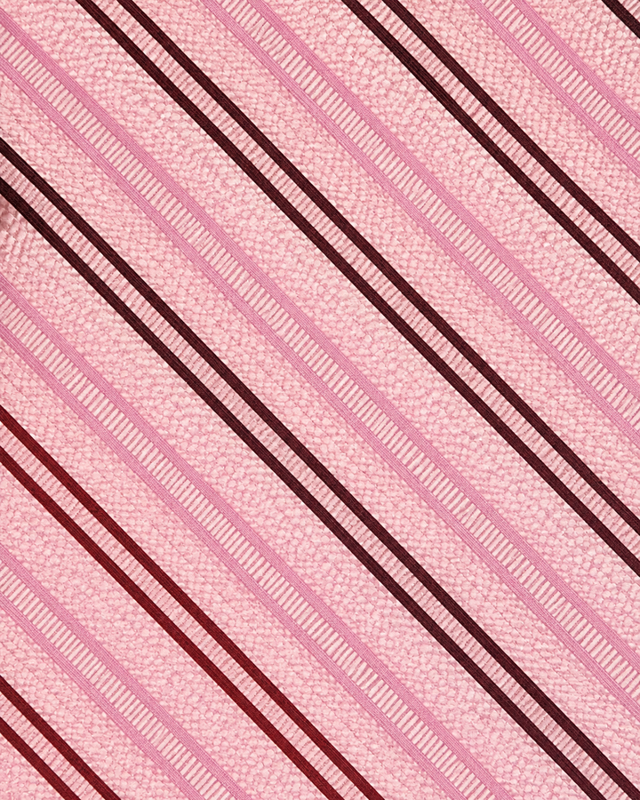 Närbild av parvisa mörka diagonala band och smalare rosa accentband på ljusrosa botten på JOTA, bröstnäsduk i ljusrosa, svart och mörkrosa