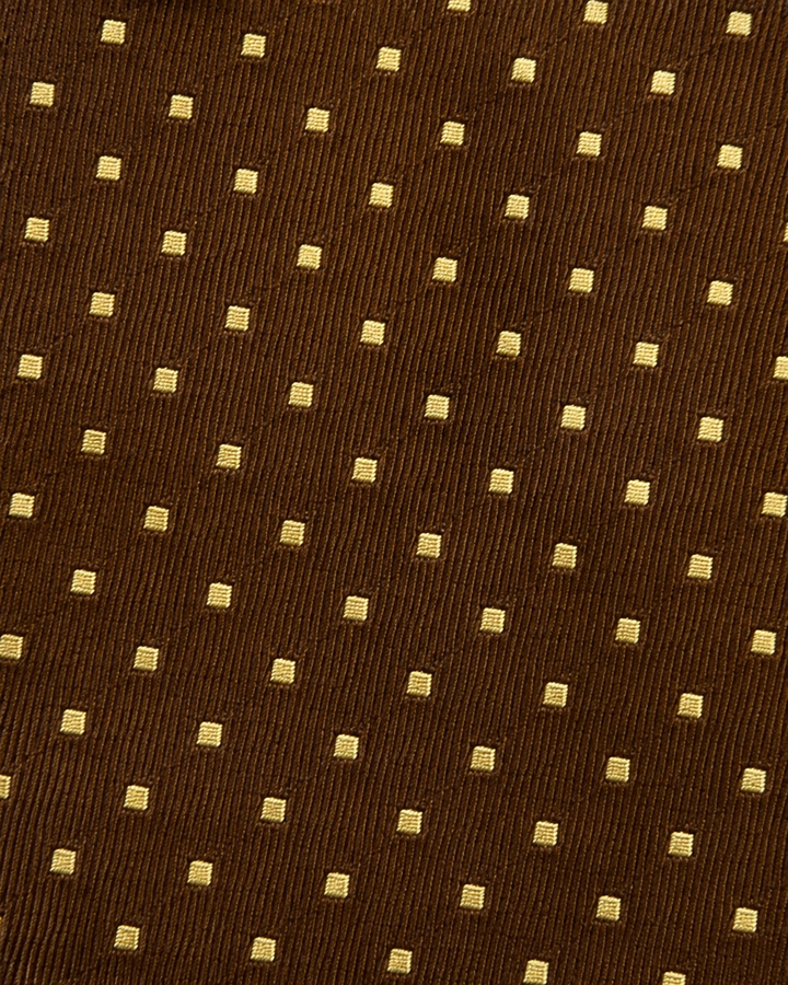 Närbild av framträdande gula prickar över en diskret randstruktur på brun botten på JUBA, bred slips i brunt och gult