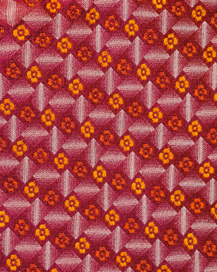 Närbild av ett tätt upprepat orange- och guldfärgat blomdiamantmotiv på mörk orange-röd botten på JUSTITIA, bred slips i orange, rött och guld