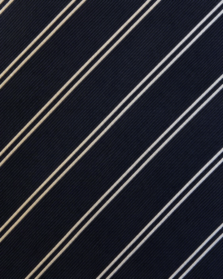 Närbild av en bred silverfärgad diagonal rand med fina ljusa diagonala linjer emellan på TRITON, bred slips i mörkblått, silver och ljusa toner