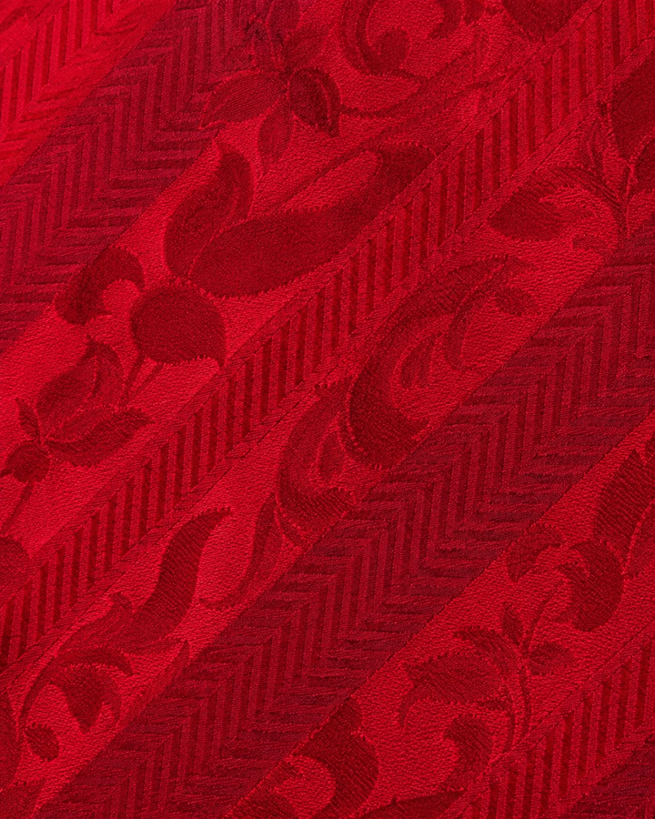Närbild av tonala röda ornamentmotiv ordnade inom diagonala band på VICTORIA SMAL, smal slips i rött i flera toner
