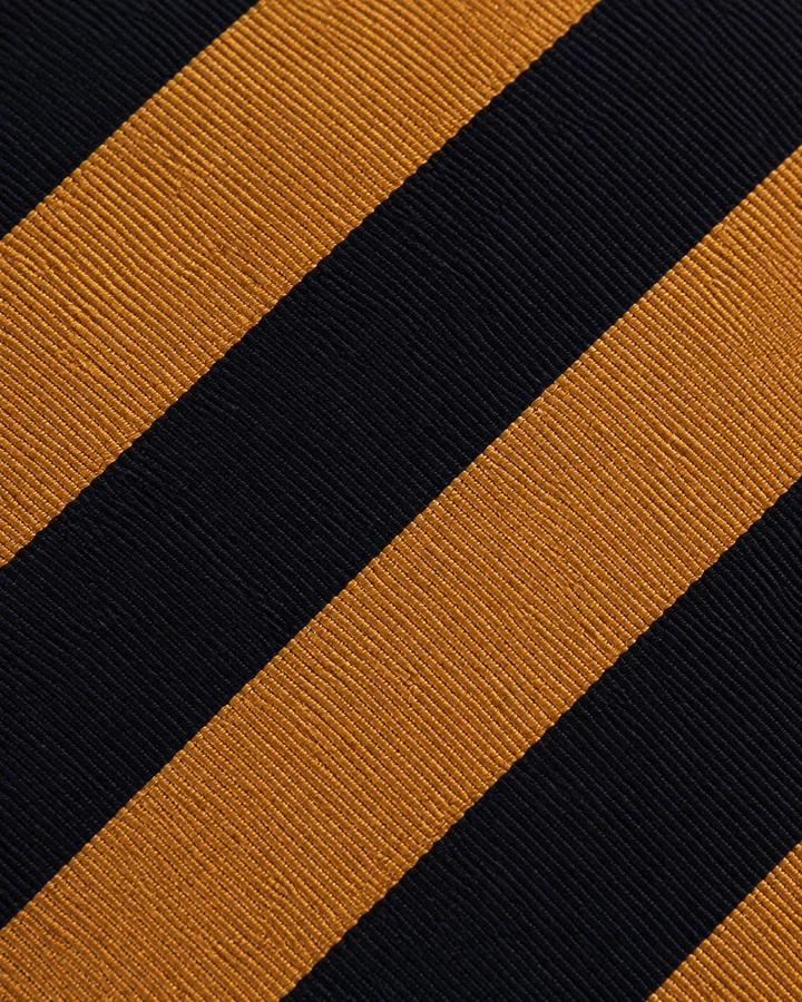Närbild av breda svarta och guldfärgade diagonala band på YMIR, bred slips i svart och guld